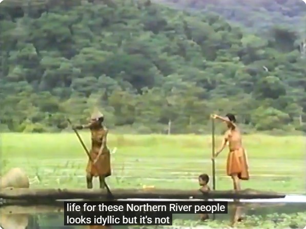 Deux femmes pagayent sur la rivière Sepik avec un enfant à bord de leur canoë. La légende indique: la vie semble idyllique mais ce n'est pas le cas.