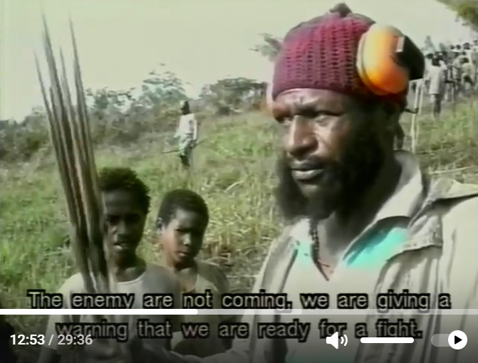 Un guerrier papou explique devant deux enfants qu'ils sont prêts à donner une leçon à l'ennemi.