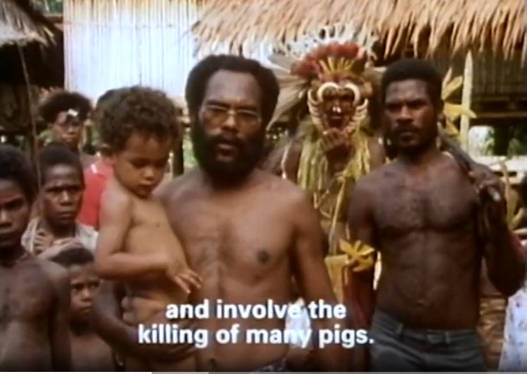 John Waiko porte son fils Bao devant les membres de sa tribu. Le sous-titre dit qu'il va falloir tuer beaucoup de cochons.