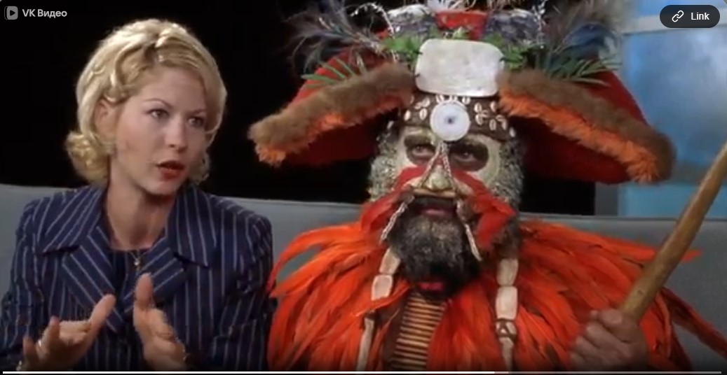 La chercheuse Veronica (Jenna Elfman) présente James Krippendorf (Richard Dreyfuss), déguisé en chef papou, sur un plateau de télévision.