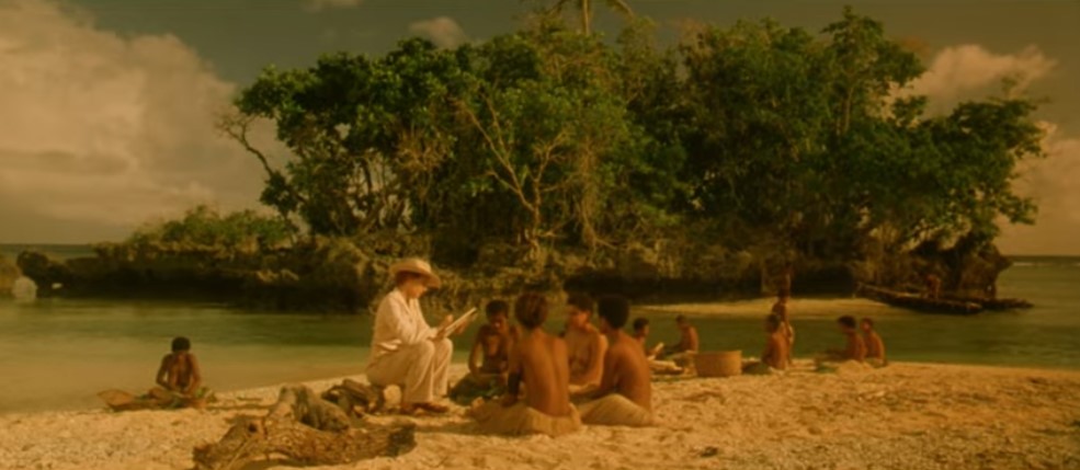 Devant un îlot verdoyant, l'anthropologue Evelyn Spence (Maya Stange) discute sur la plage avec les jeunes filles trobriandaises et prend des notes.