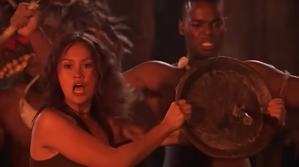 L'aventurière Sydney Fox (Tia Carrere) arrête avec un bouclier le poignard qui menaçait le guerrier papou Mudo (Demore Barnes).