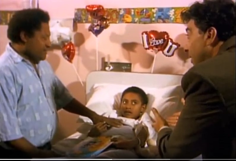 L'enfant Ashira (Anthony Gabb) est veillé sur son lit d'hôpital par son père Douglas (Douglas Gabb) et par le journaliste Martin (Tiriel Mora).