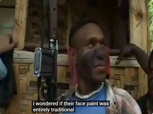 Un combattant papou avec son fusil automatique a le visage peint en noir à la façon de Rambo.