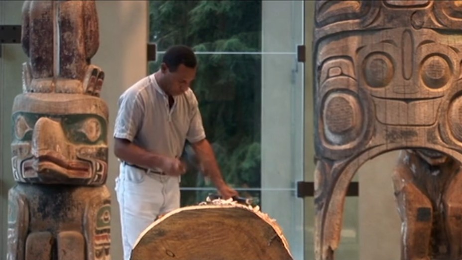 Le sculpteur papou Teddy Balangu, entouré de totems salishes des Indiens du Canada, taille avec ses outils un tronc d'arbre pour en faire son œuvre Tuwatmeri Pole.
