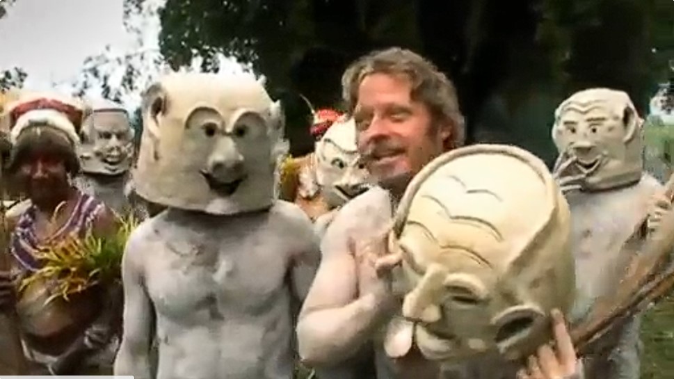 Charley Boorman couvert de boue tient un masque rituel au milieu de membres de la tribu Asaro des hautes-terres de Papouasie-Nouvelle-Guinée.