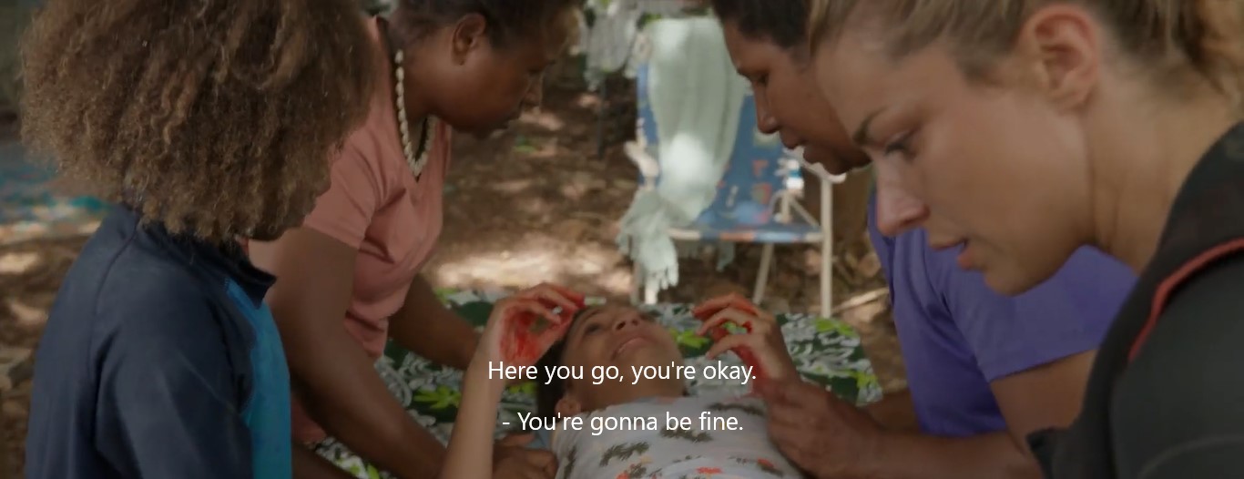 Au campement près de la plage, Winston (Barney Ling), Betty (Sophie Naime), Tara (Wendy Mocke) et Nic (Teressa Liane) secourent la jeune Demi (Eva Mocke-Kanaki), allongée les mains pleines de sang sur une table couverte d'un paréo.