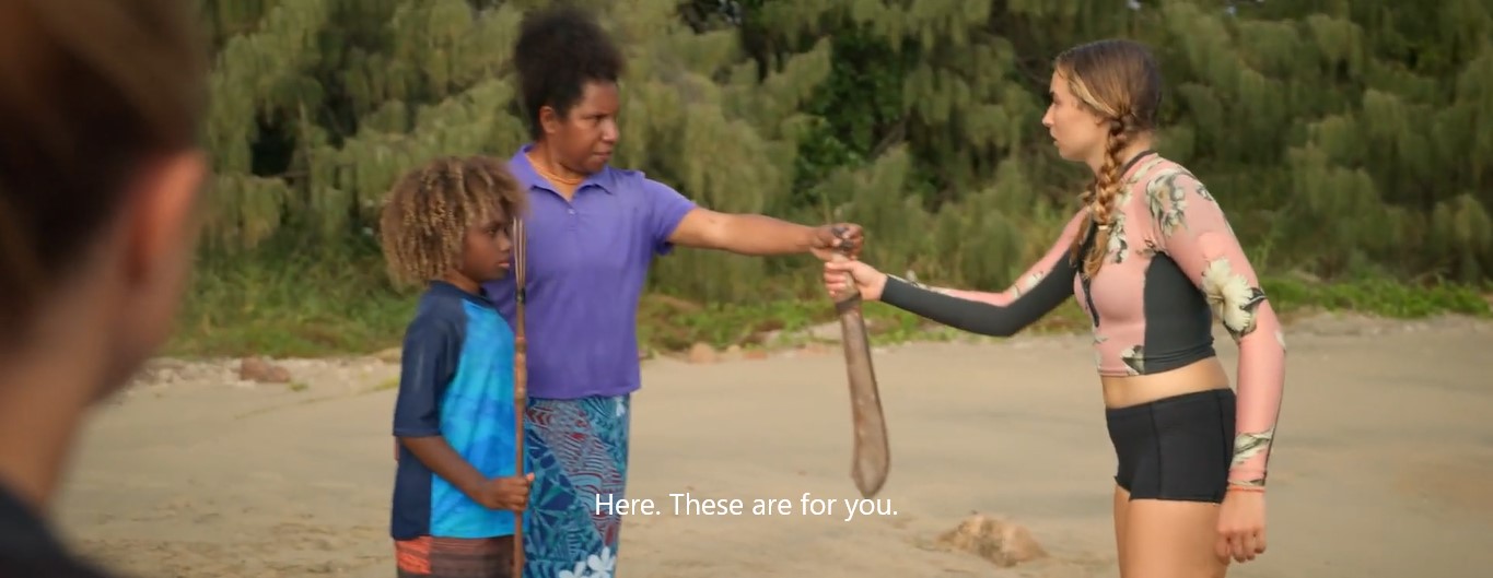 Sur la plage, Tara (Wendy Mocke), en compagnie de son fils Winston (Barney Ling) porteur d'un trident, donne une machette pour se défendre à Annie (Saskia Archer), sous le regard de sa sœur Nic (Teressa Liane).